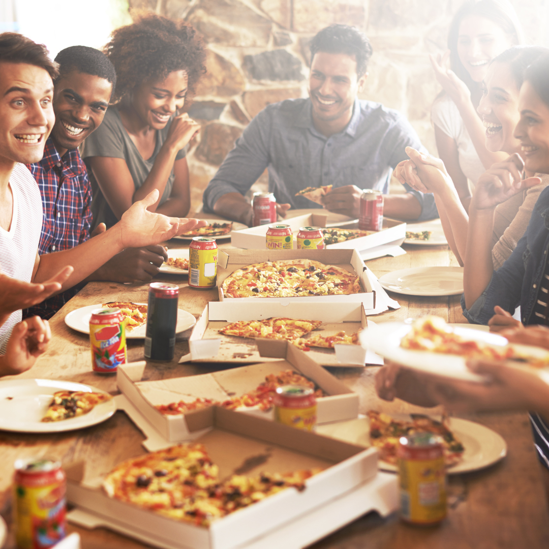 Many people sit at a table talking and laughing with pizzas and beer.